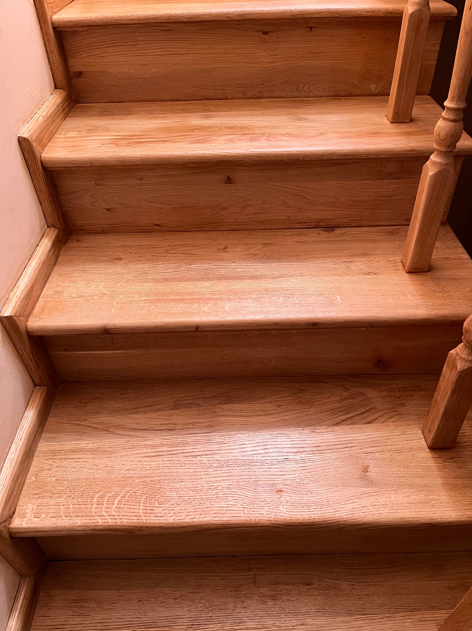 Jasne, drewniane schody z balustradą, widok z dołu. Naturalne wykończenie drewna, ciepłe oświetlenie. Detal poręczy i stopni.