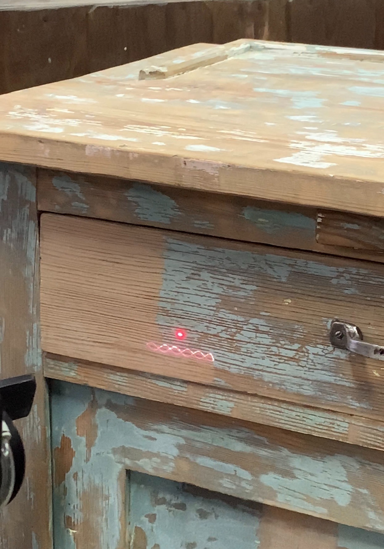 Fragment komody w stylu vintage, z widocznymi śladami użytkowania i laserowo czyszczonym fragmentem szuflady, ukazującym różnicę w wyglądzie.