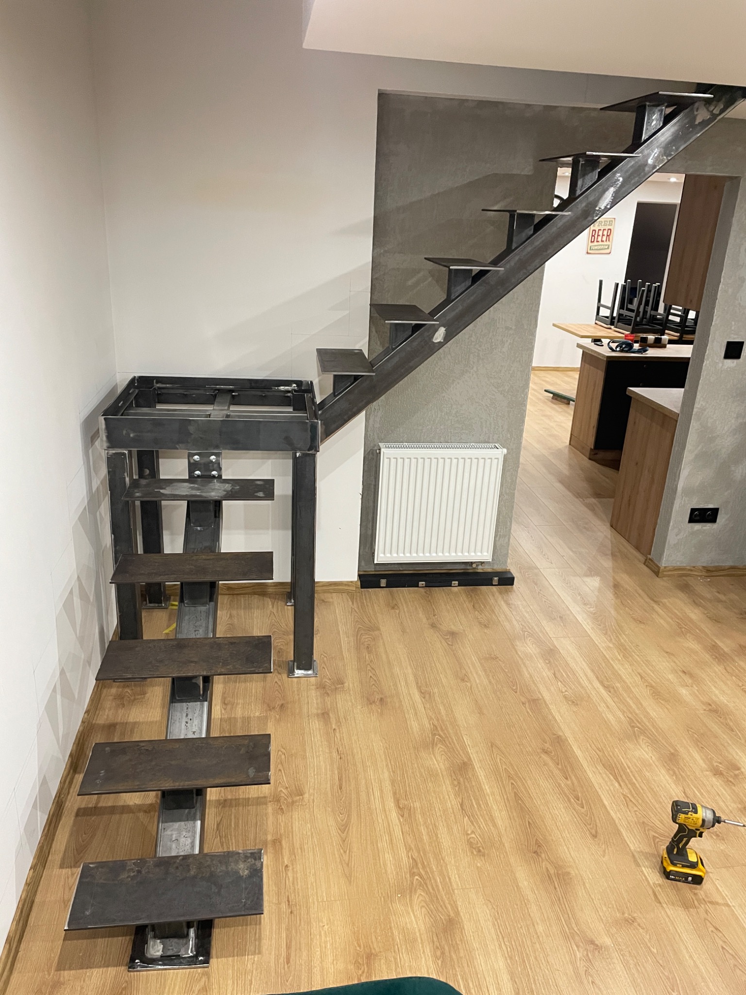 Surowe, metalowe schody z przyspawanymi stopniami w trakcie montażu wewnątrz budynku. Widoczny spaw i narzędzia, surowy beton na ścianie.