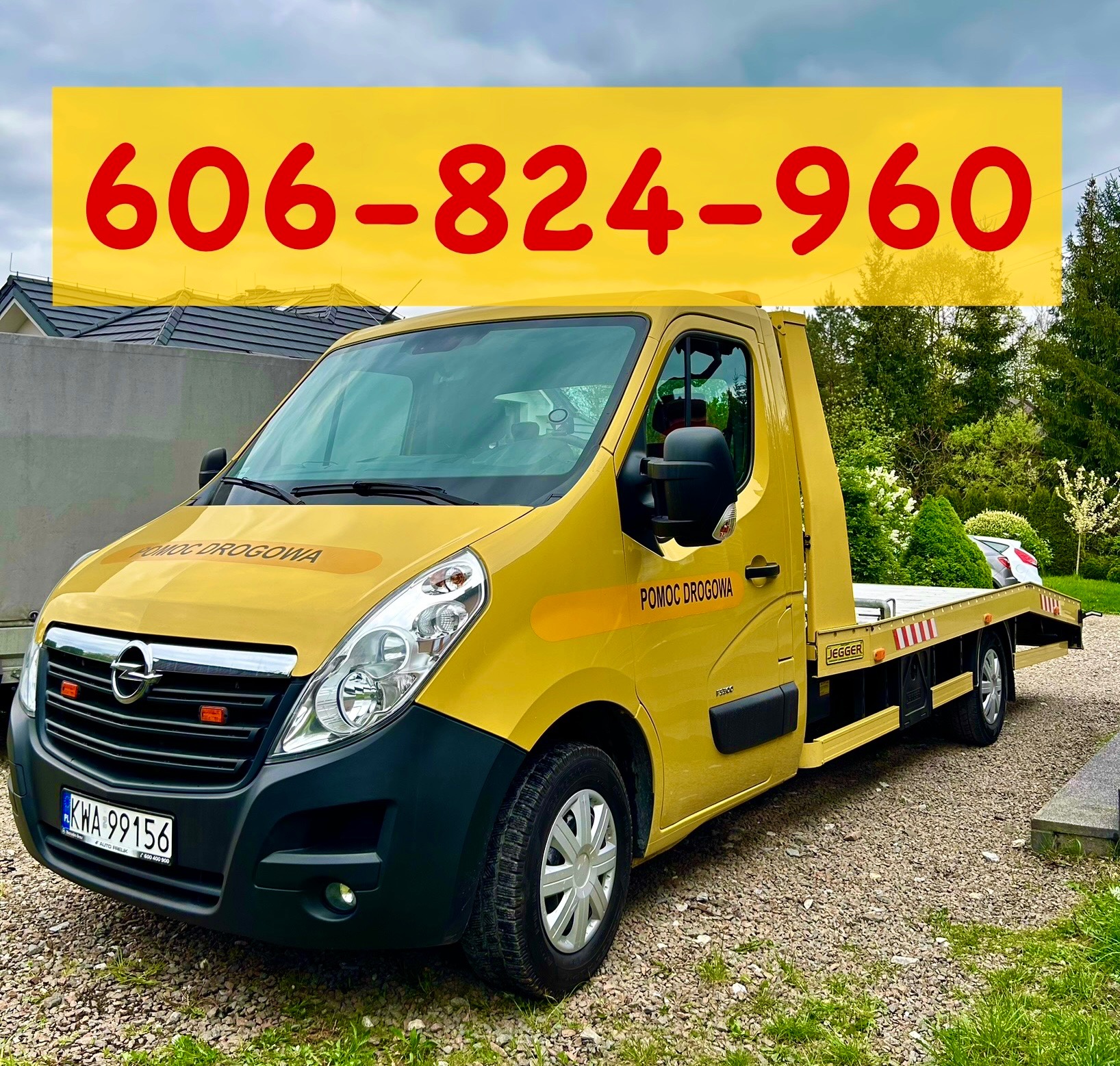 Żółta laweta Opel z napisem 'Pomoc Drogowa' i numerem telefonu na tle zieleni i zabudowań. Na platformie lawety stoi uszkodzony, srebrny samochód osobowy.