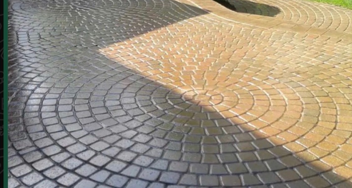 Częściowo umyta, okrągła kostka brukowa w odcieniach szarości i beżu, ułożona w koncentryczne kręgi. Widoczny efekt czyszczenia pod ciśnieniem.