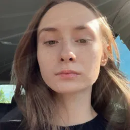 Portret kobiety z bliska, z naturalnym makijażem i promieniami słońca padającymi na twarz, uchwycony wewnątrz samochodu.