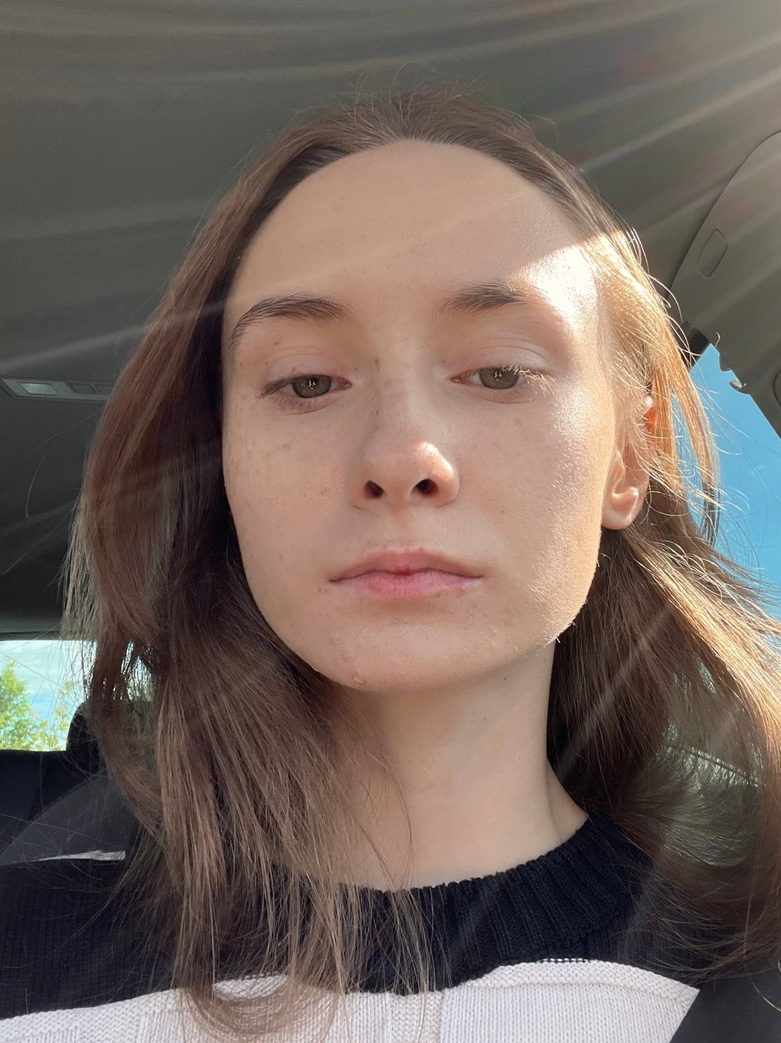 Portret kobiety z bliska, z naturalnym makijażem i promieniami słońca padającymi na twarz, uchwycony wewnątrz samochodu.