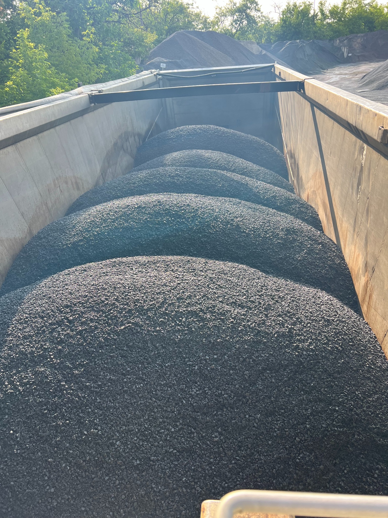 Kopalnia kruszywa: Widok z góry na naczepę wypełnioną czarnym, drobnym kamieniem. W tle widać hałdy materiału i zieleń drzew.