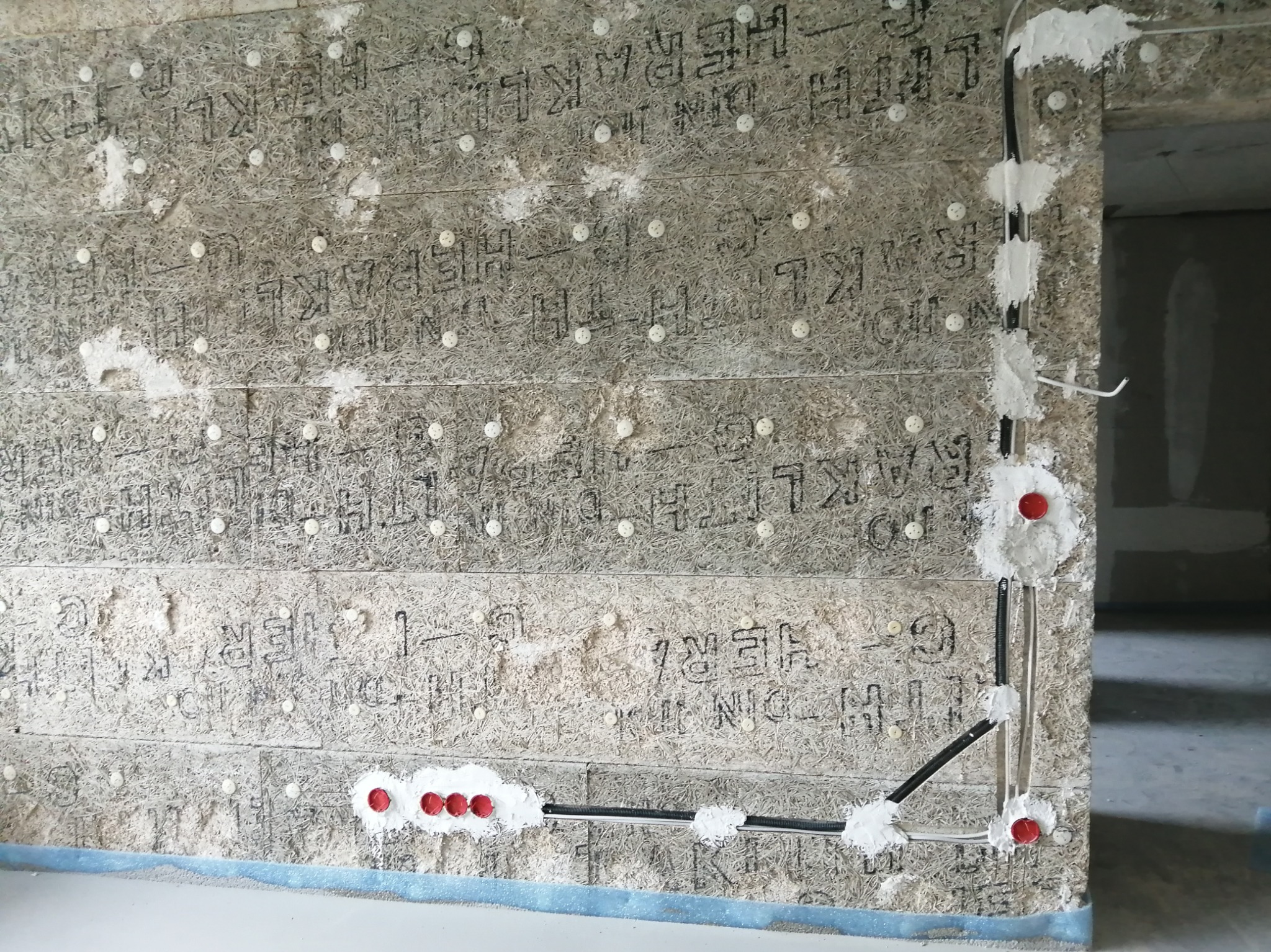 Ściana z izolacją, w której poprowadzone są kable elektryczne zabezpieczone pianką montażową i puszkami. Widoczne otwory pod gniazdka.