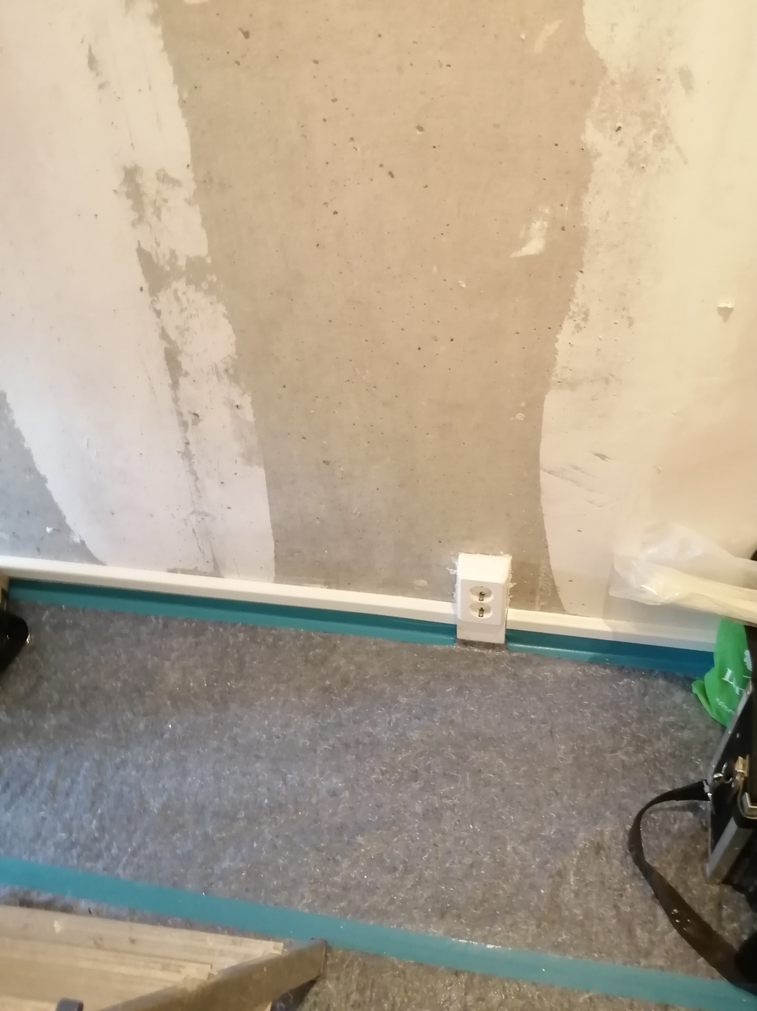 Białe gniazdko elektryczne zamontowane przy podłodze w pomieszczeniu w trakcie remontu. Widoczne ślady po szpachlowaniu na ścianie.