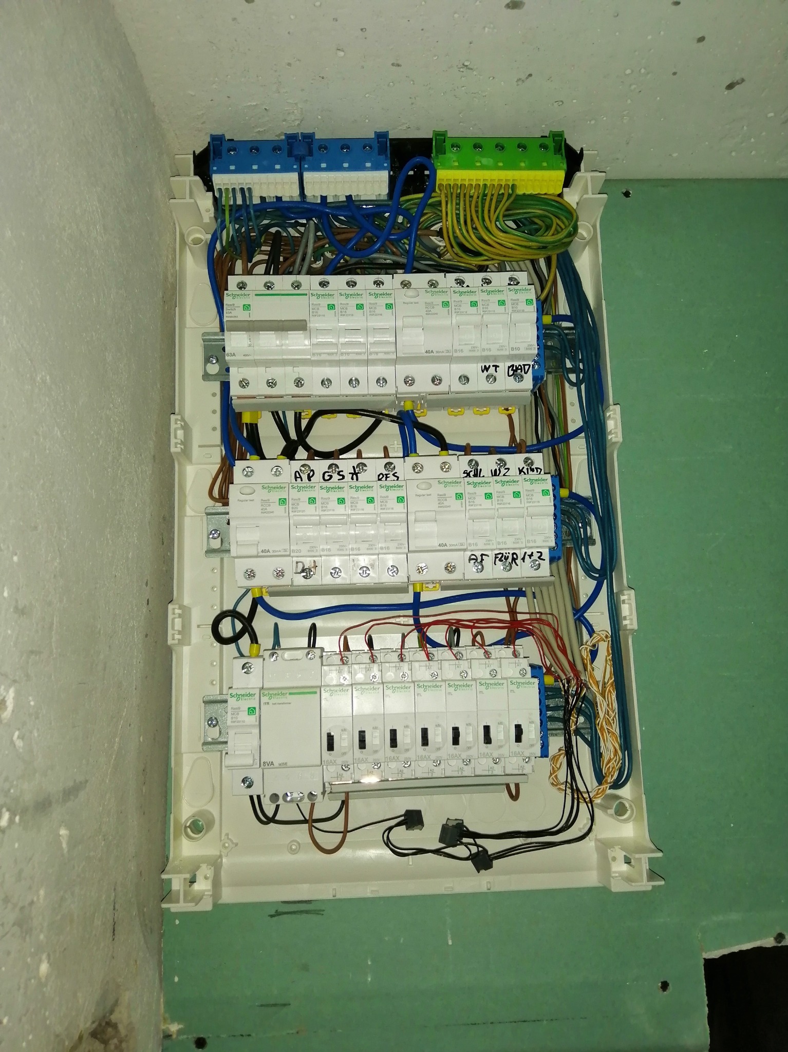 Rozdzielnia elektryczna Schneider z bezpiecznikami i okablowaniem, zamontowana na ścianie. Widoczne detale instalacji i oznaczenia.