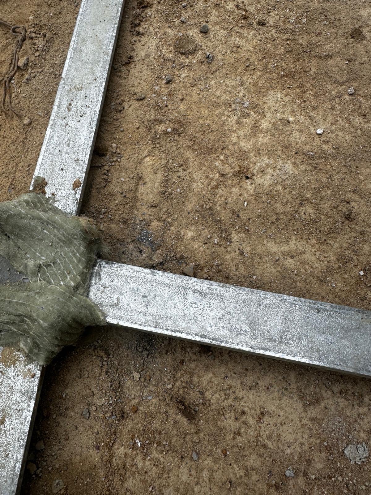 Fragment konstrukcji z metalowych profili, połączonych materiałem izolacyjnym, na tle ziemi. Widoczne ślady spawania. Detal instalacji.