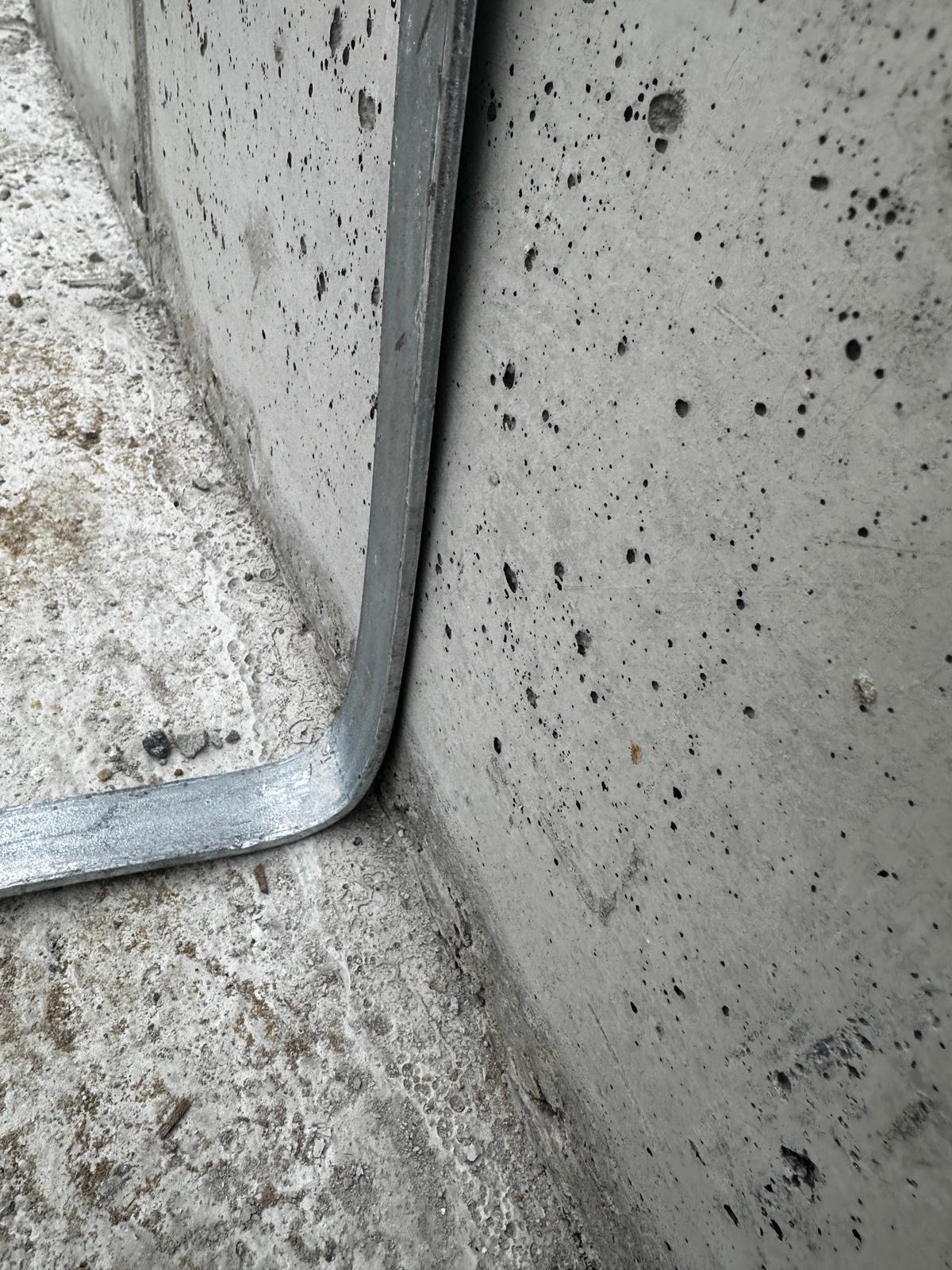 Szara, metalowa listwa na surowym betonie, zabezpieczenie budynku w Zacharzycach. Element instalacji elektrycznej na zewnątrz budynku.