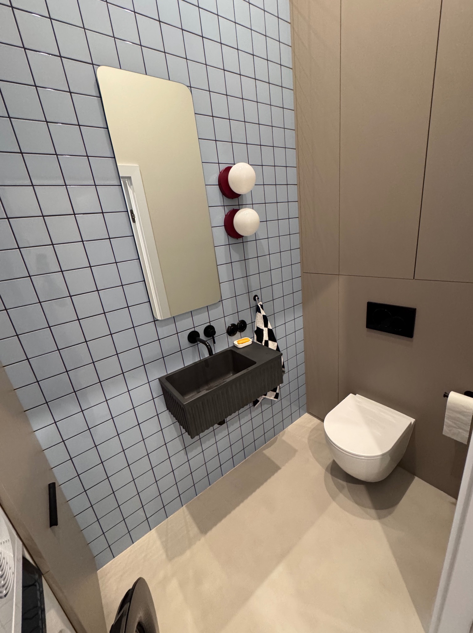 Nowoczesna łazienka: błękitne płytki z ciemną fugą, grafitowa umywalka, minimalistyczne oświetlenie i toaleta podwieszana w beżowej zabudowie.