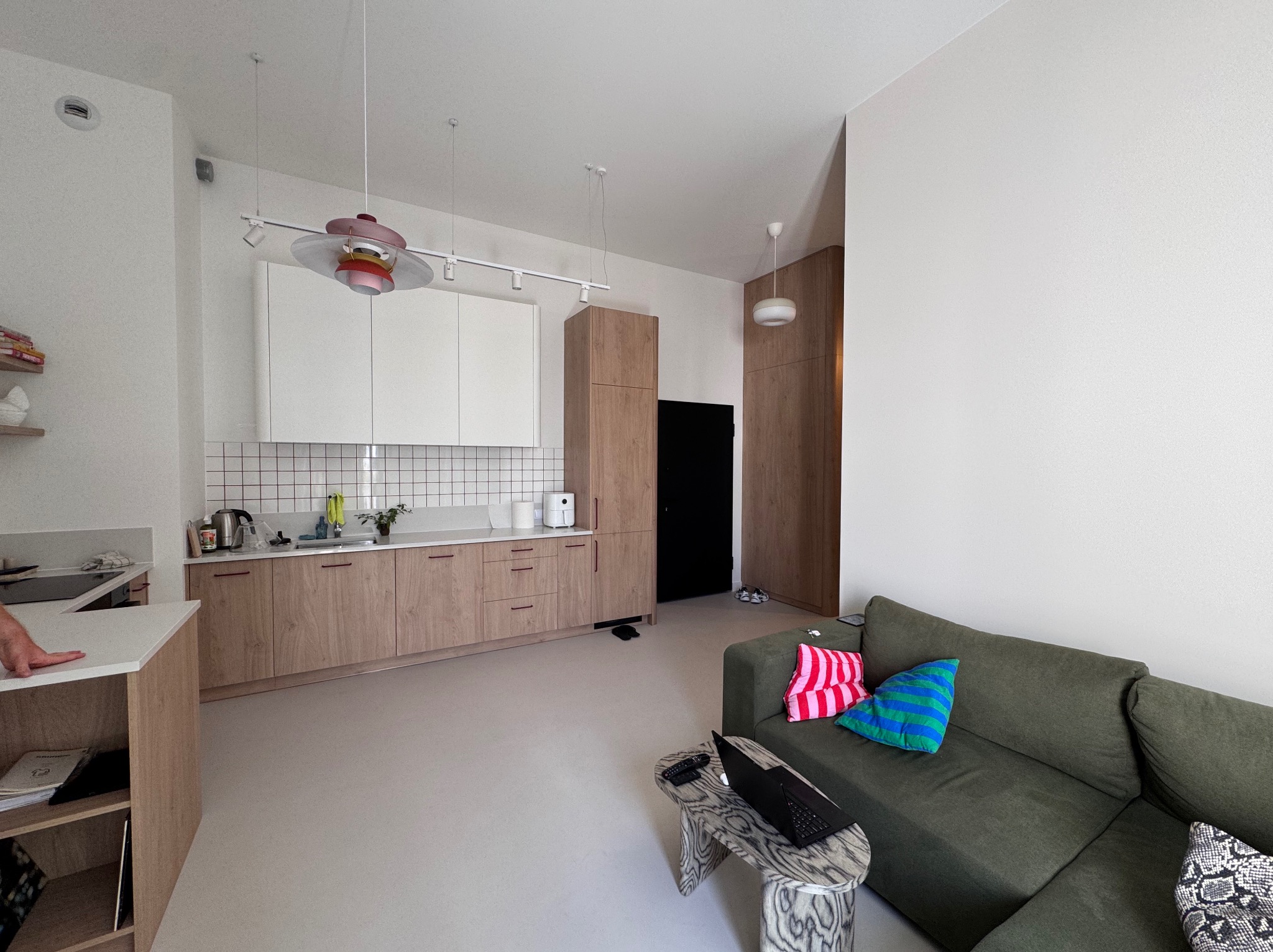 Jasne wnętrze: kuchnia z drewnianymi szafkami i białymi płytkami, salon z zieloną sofą i wzorzystym stolikiem. Minimalistyczny design, nowoczesne oświetlenie.