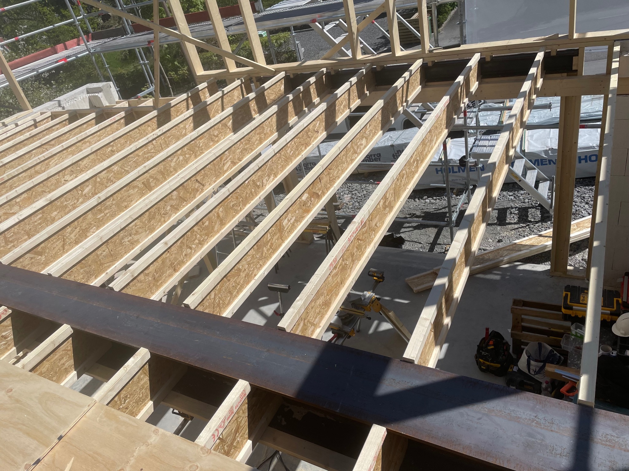 Konstrukcja stropu z belek dwuteowych i płyt OSB w trakcie budowy domu szkieletowego. Widoczne narzędzia i materiały budowlane.