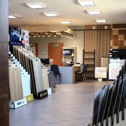 MDR SALON DRZWI PODŁÓG PŁYTEK SPÓŁKA Z OGRANICZONĄ ODPOWIEDZIALNOŚCIĄ - Ekspozycja paneli podłogowych i płytek w salonie w Koninie. Widoczne wzorniki różnych producentów, biuro obsługi klienta i oświetlenie sufitowe.