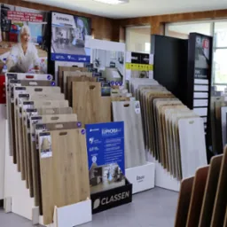 Ekspozycja paneli podłogowych w sklepie: różnorodne wzory i kolory, od jasnych po ciemne, z widocznymi oznaczeniami producentów i kolekcji, takich jak Classen Euphoria 4V.