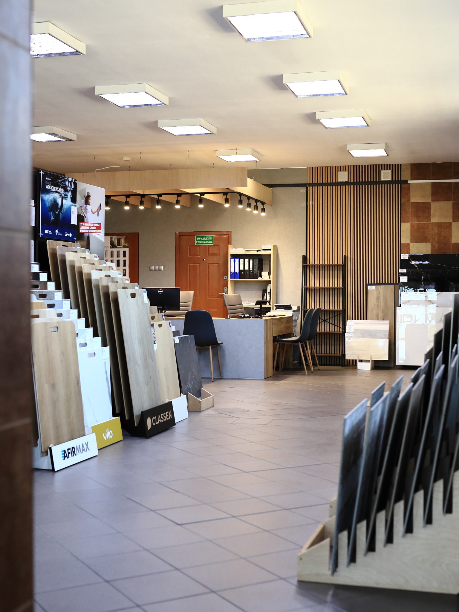 Ekspozycja paneli podłogowych i płytek w salonie w Koninie. Widoczne wzorniki różnych producentów, biuro obsługi klienta i oświetlenie sufitowe.