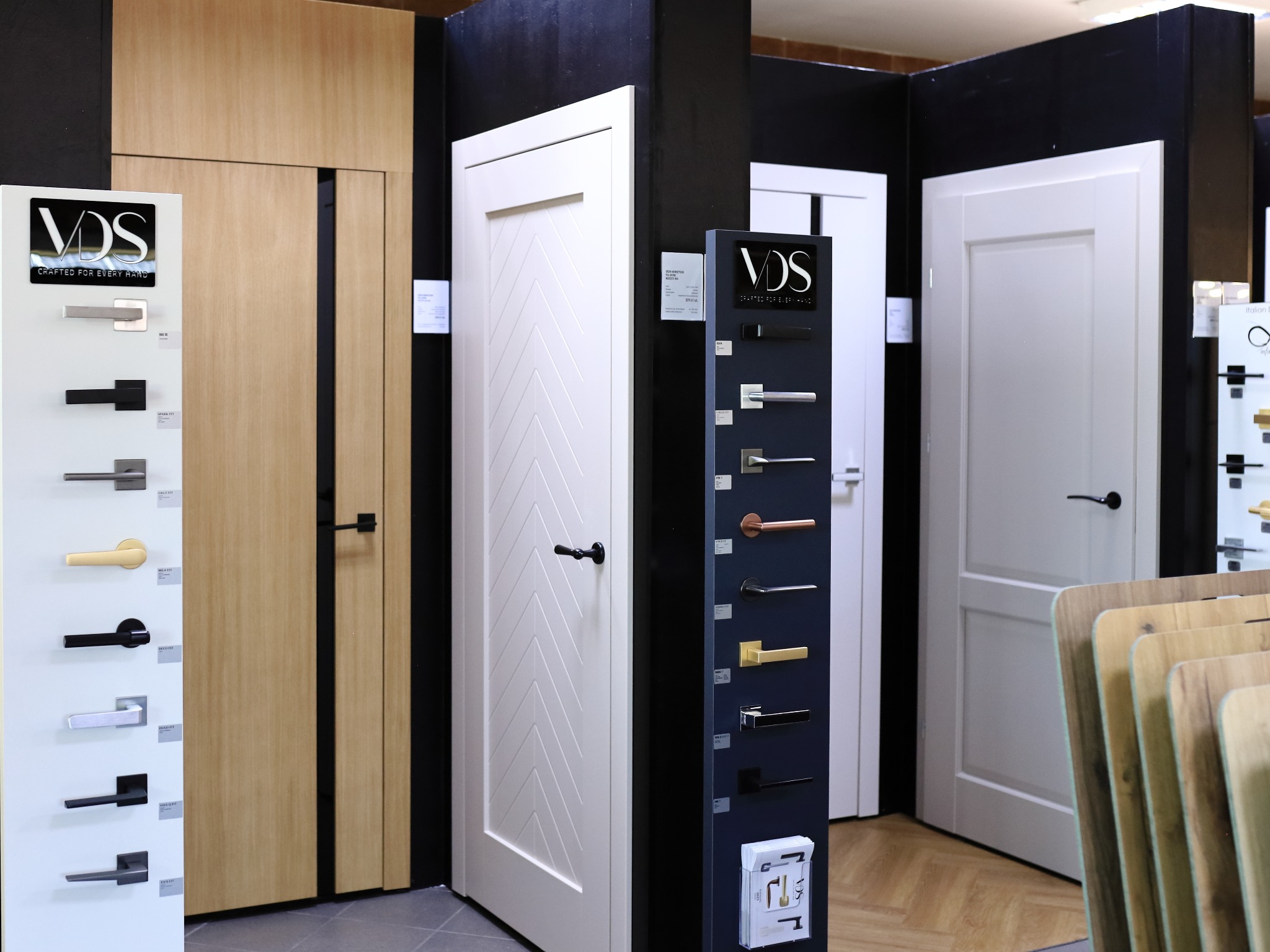 Ekspozycja drzwi wewnętrznych i klamek w salonie. Widoczne modele w różnych stylach, od klasycznych po nowoczesne, wraz z katalogami klamek.