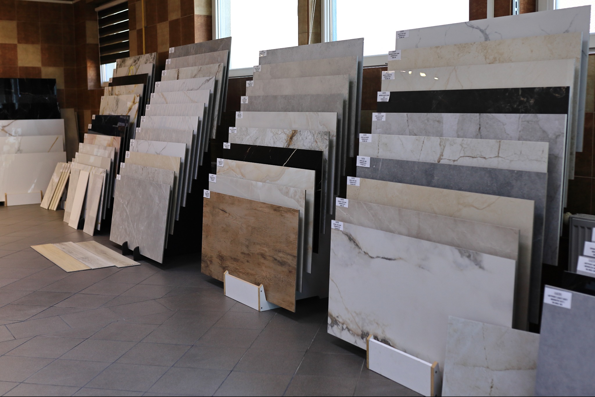 Ekspozycja płytek podłogowych i ściennych w sklepie: różnorodne wzory, kolory i faktury, od imitacji drewna po marmurkowe wykończenia. Jasne oświetlenie, nowoczesny design.