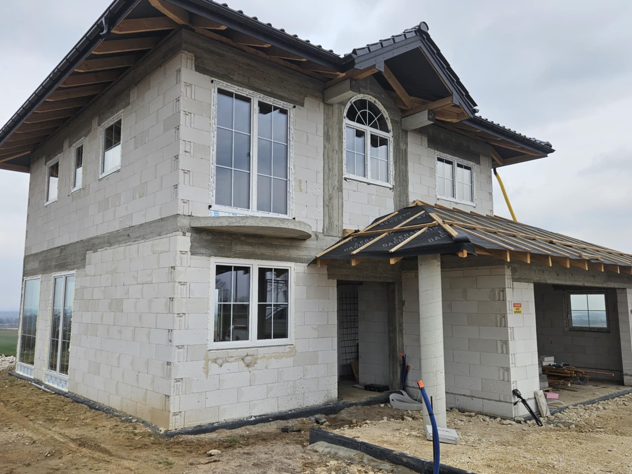 Dom w stanie surowym otwartym z zamontowanymi oknami PCV o białych ramach i różnej wielkości, z widocznymi elementami konstrukcji dachu.