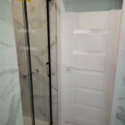 Nowoczesna łazienka z kabiną prysznicową w czarnej ramie i białą, panelową  drzwi. Marmurowe płytki na ścianach i podłodze. Minimalistyczny design.