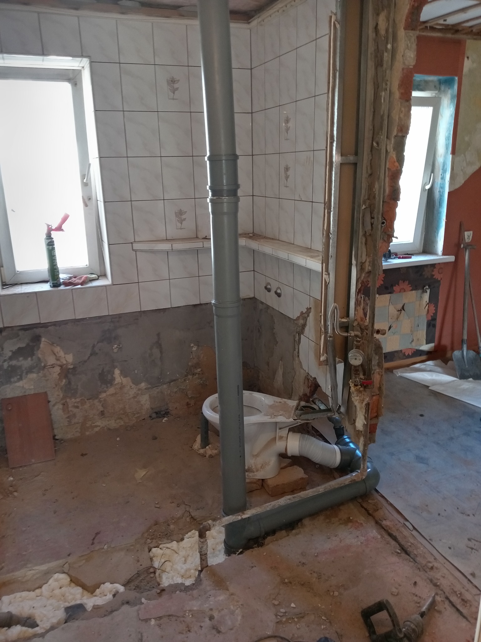 Demontaż instalacji w łazience przed remontem: widoczne rury kanalizacyjne, fragment toalety, ślady po płytkach na ścianach, gruz i narzędzia.