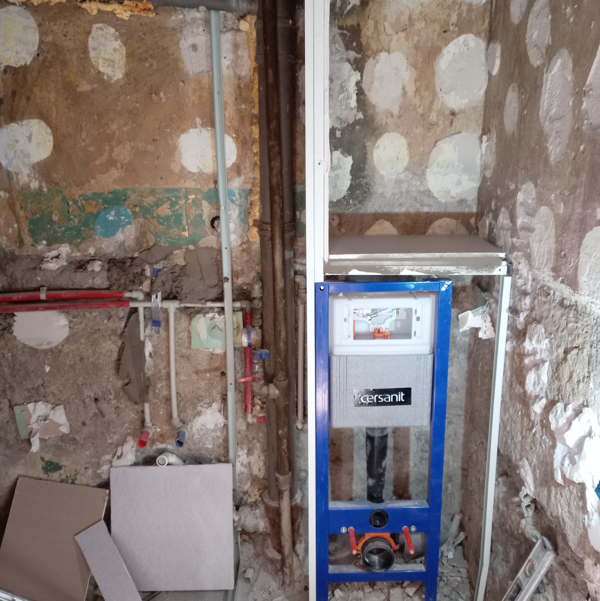 Stelaż podtynkowy Cersanit w łazience w trakcie remontu. Widoczne rury, instalacje i surowe ściany z resztkami farby. Etap prac przed wykończeniem.
