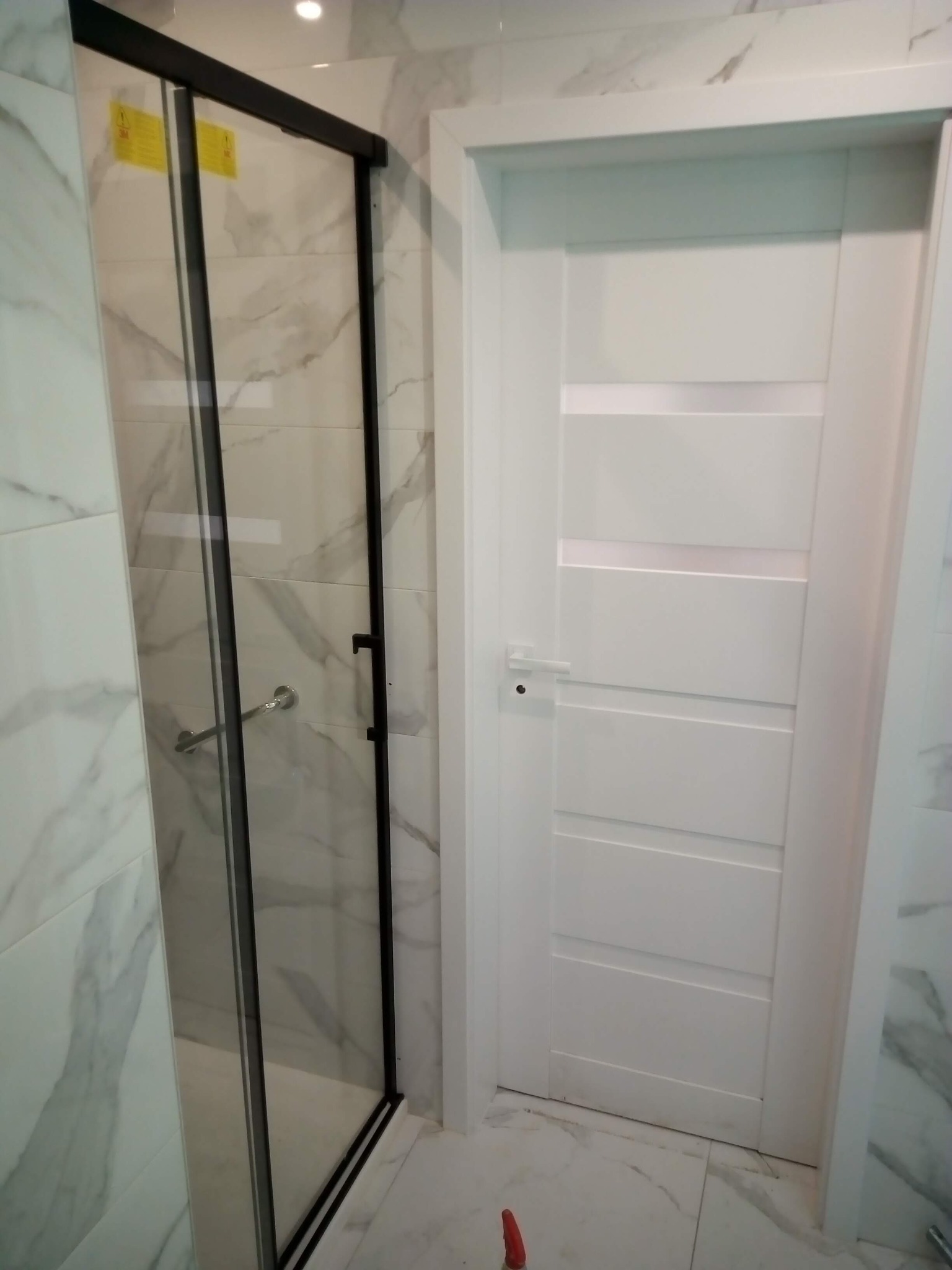 Nowoczesna łazienka z kabiną prysznicową w czarnej ramie i białą, panelową  drzwi. Marmurowe płytki na ścianach i podłodze. Minimalistyczny design.