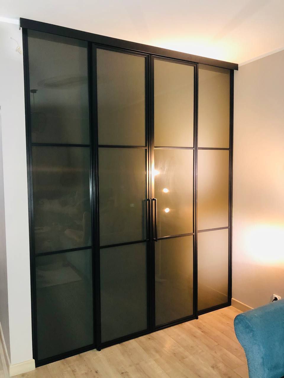 Eleganckie, czteroskrzydłowe drzwi przesuwne z matowego szkła i czarnych szprosów, oddzielające pomieszczenia w nowoczesnym wnętrzu. Widoczny fragment podłogi.