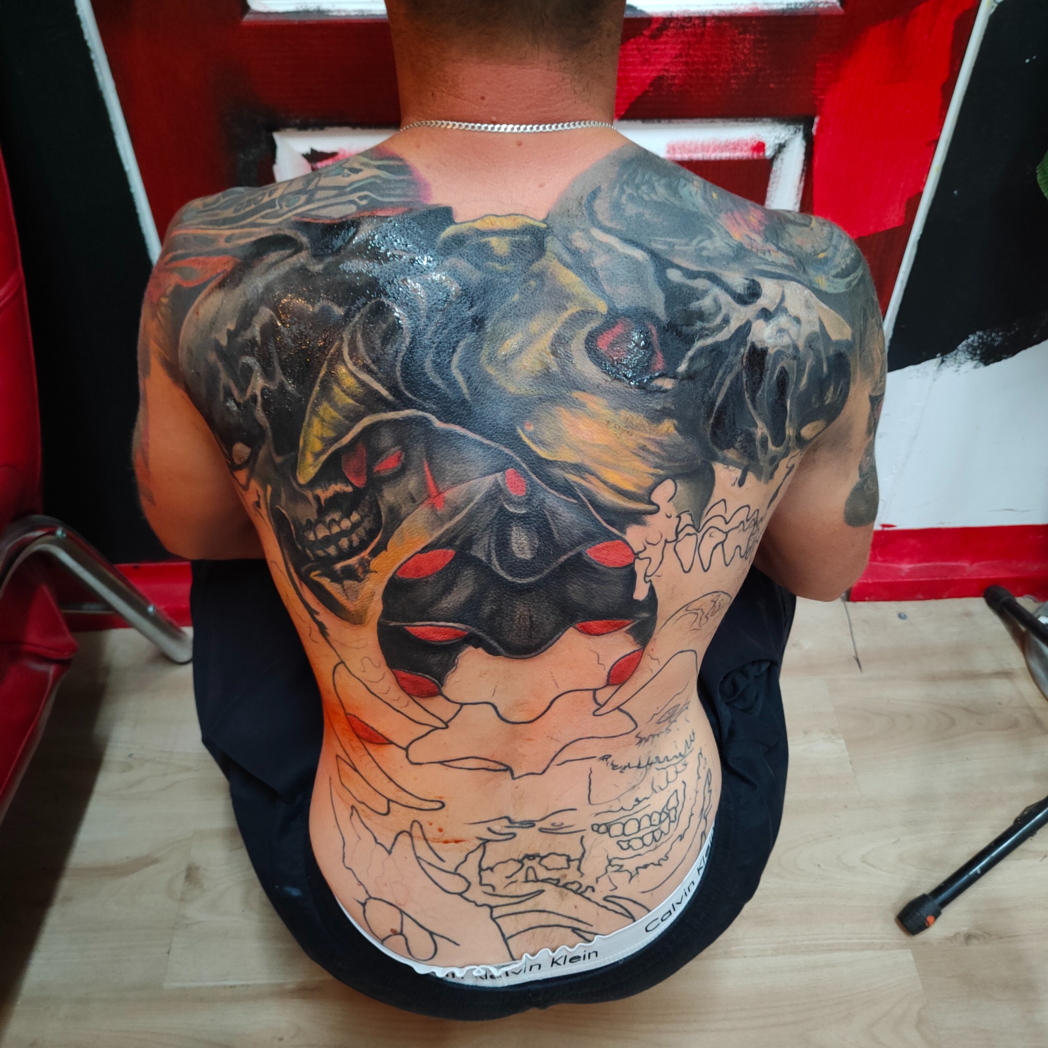 Mężczyzna z rozbudowanym tatuażem na plecach, częściowo w trakcie wykonywania. Widoczny etap tworzenia wzoru, kontrast między gotowym a szkicem.