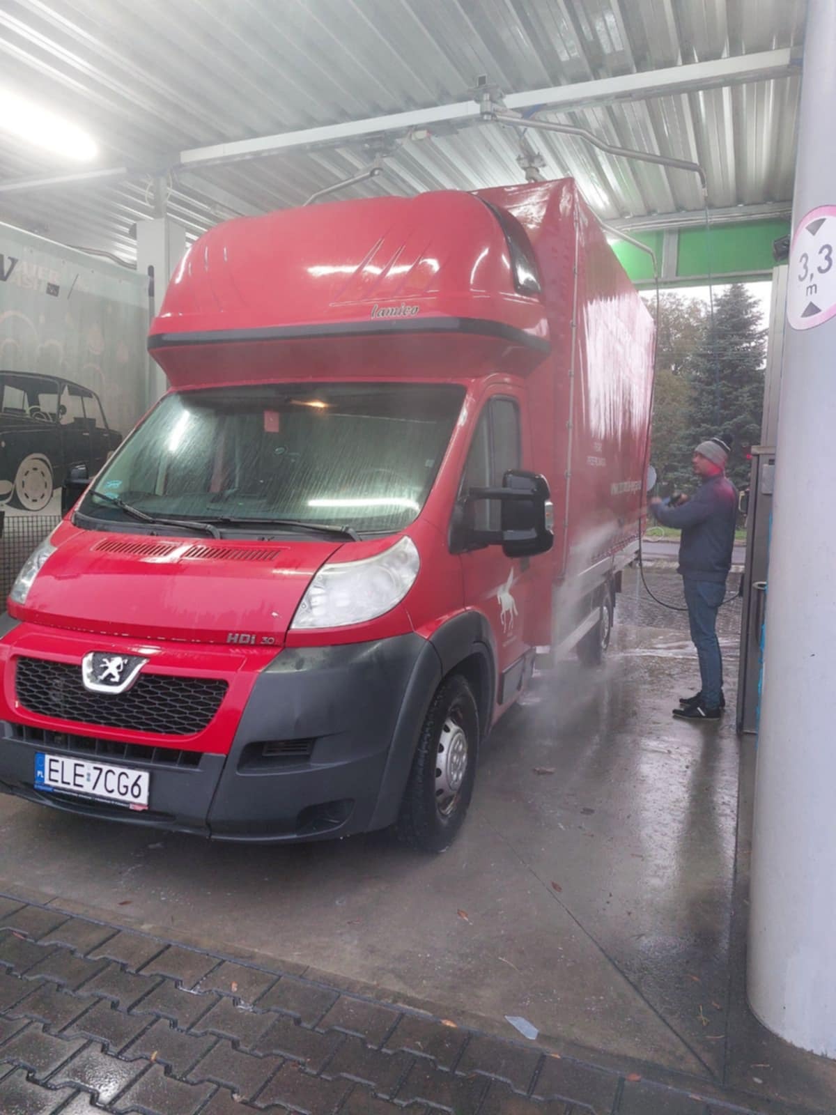 Czerwony samochód dostawczy marki Peugeot myty w myjni w Łodzi. Na boku widoczne logo firmy transportowej z wizerunkiem konia. Osoba myje auto lancą.