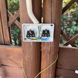 Antoni Mazurkiewicz - Otwarta puszka elektryczna z podłączonymi przewodami na drewnianej konstrukcji altany. Widoczne złącza i fragment peszla ochronnego.