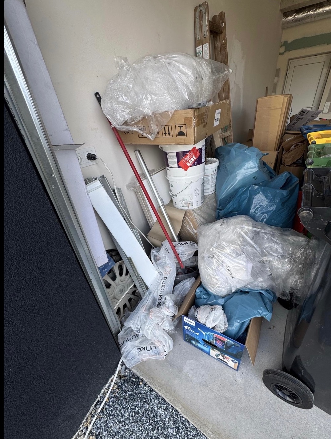 Zagracone pomieszczenie z workami, kartonami i wiadrami farby w Warszawie. Widoczny fragment opony i drabina. Opróżnianie i utylizacja.