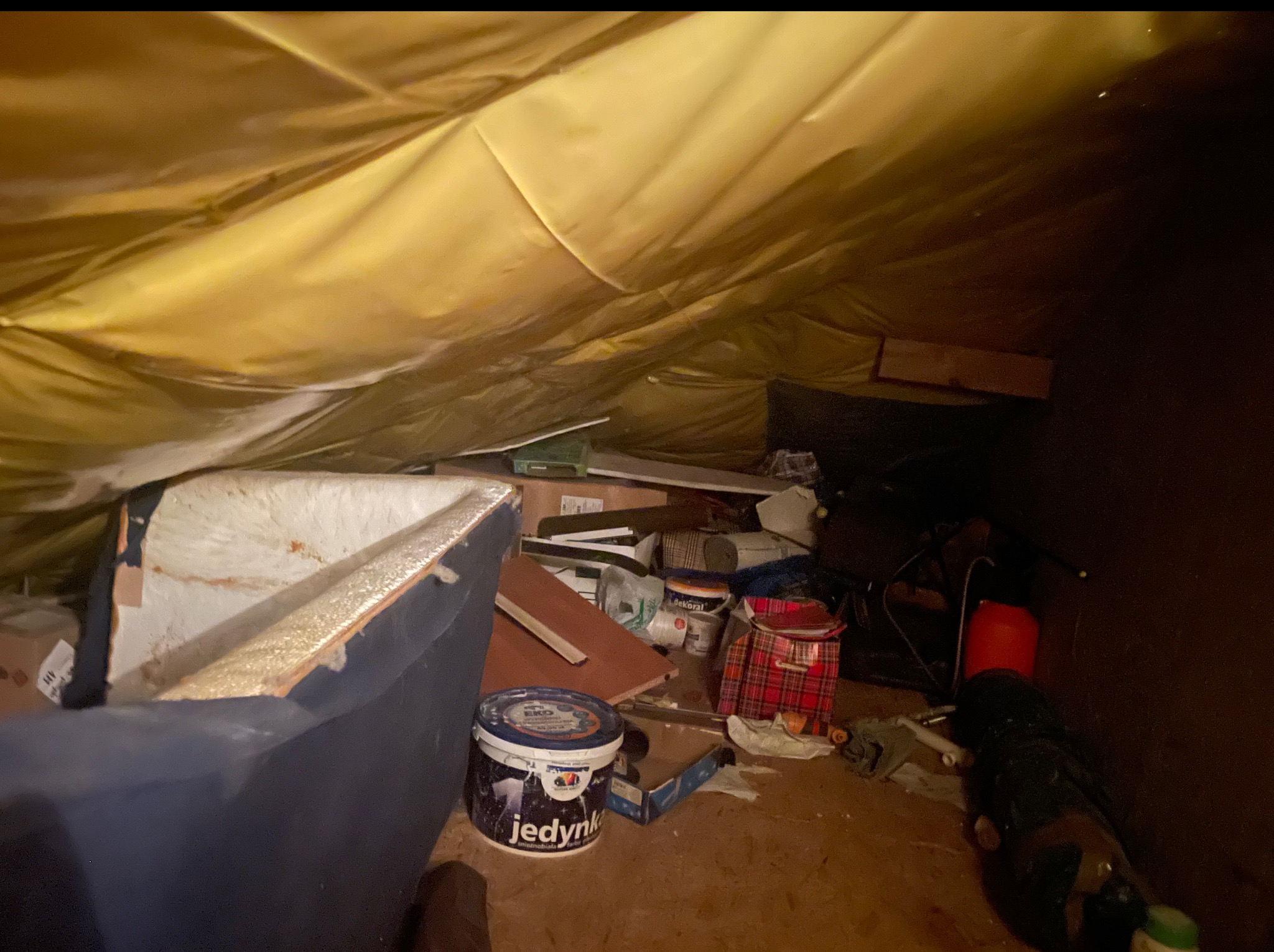 Zagracone poddasze ze skosami, widoczne stare meble, farby i inne przedmioty. Nieuporządkowana przestrzeń przed generalnym uprzątnięciem.