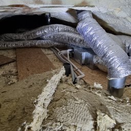 Sylwester Cymborski - Srebrne przewody wentylacyjne klimatyzacji zamontowane pod sufitem, z widoczną izolacją termiczną i elementami konstrukcyjnymi budynku.