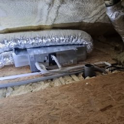 Sylwester Cymborski - Szczegółowe ujęcie instalacji klimatyzacji w przestrzeni poddasza z izolacją piankową i fragmentem drewnianej konstrukcji.