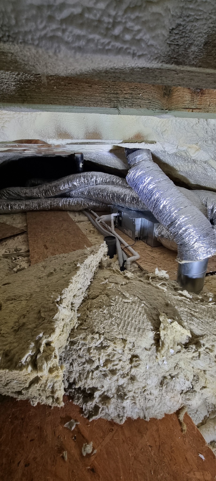 Srebrne przewody wentylacyjne klimatyzacji zamontowane pod sufitem, z widoczną izolacją termiczną i elementami konstrukcyjnymi budynku.