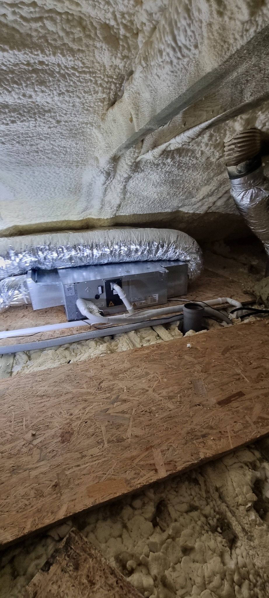 Szczegółowe ujęcie instalacji klimatyzacji w przestrzeni poddasza z izolacją piankową i fragmentem drewnianej konstrukcji.