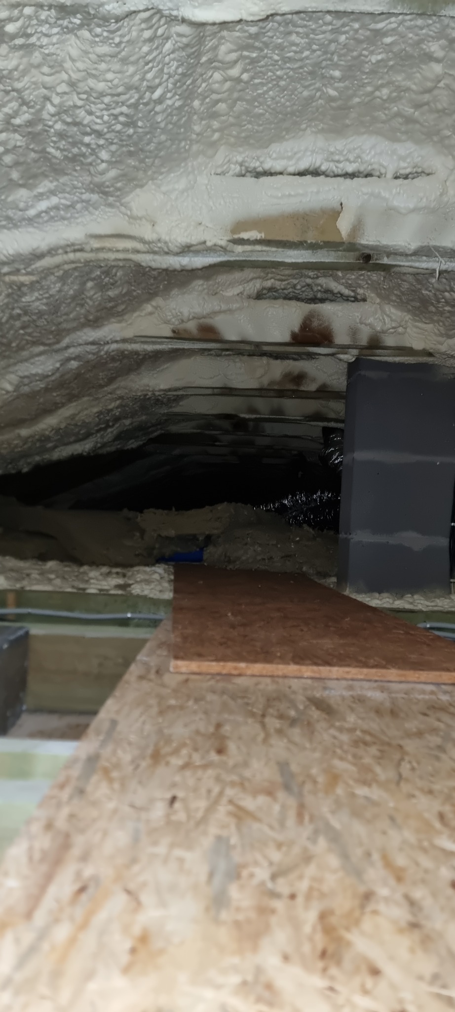 Izolacja poddasza pianką poliuretanową, widoczne elementy konstrukcyjne dachu i fragment instalacji wentylacyjnej. Detal wykończenia izolacji.