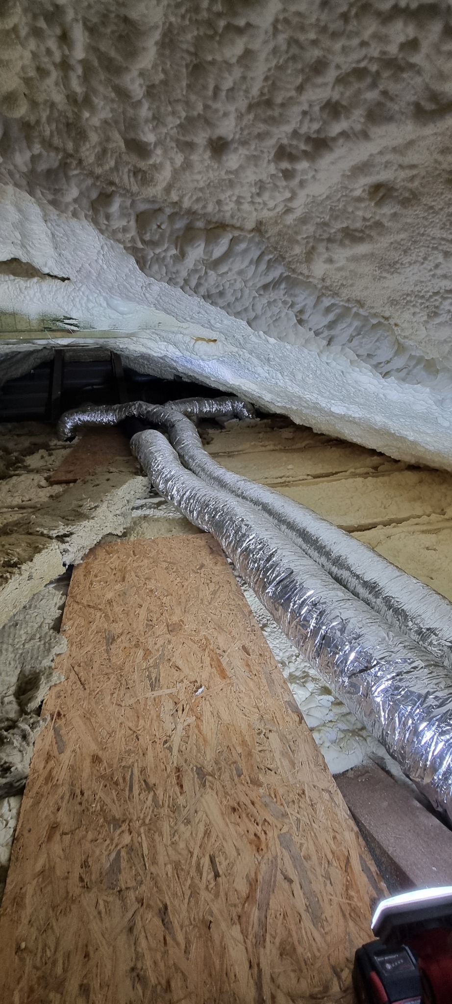 Ocieplone poddasze z widocznymi, srebrnymi rurami wentylacyjnymi i płytą OSB. Izolacja natryskowa pianką poliuretanową.