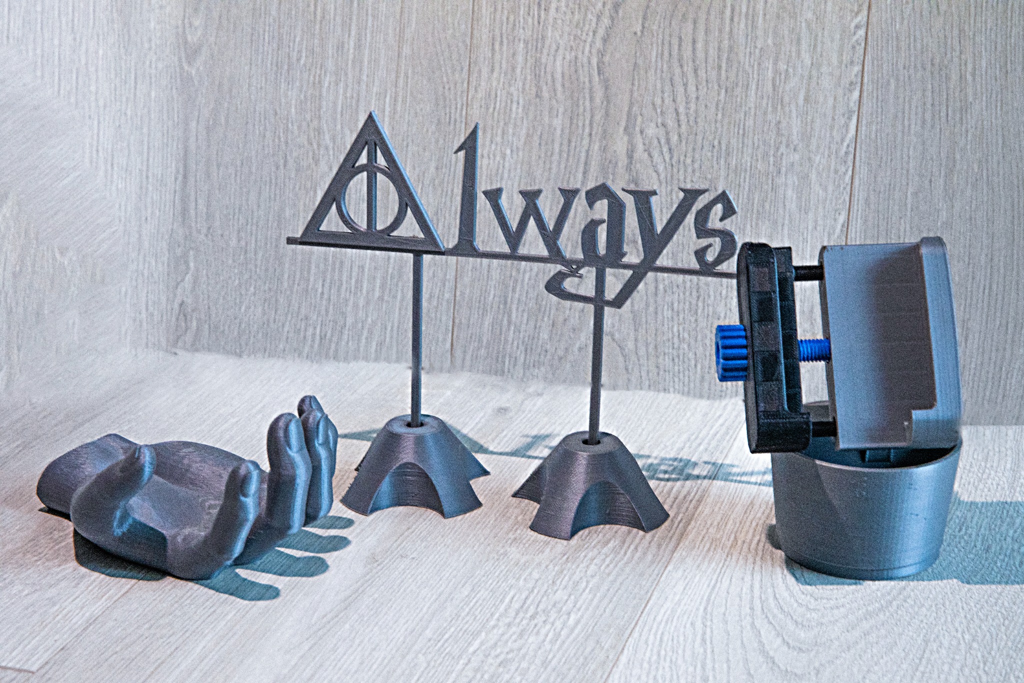 Drukowane w 3D: napis 'Always' z symbolem Insygniów Śmierci, model dłoni i narzędzie mocujące, wszystko w szarym odcieniu na jasnym tle.