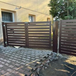 OGROTKOWO MARCIN GROTEK - Brązowa, nowoczesna brama wjazdowa z poziomymi panelami, zamontowana na posesji z kostką brukową. Widoczne ślady prac ziemnych.