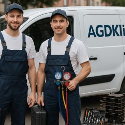 AGDKlinika - Dwóch uśmiechniętych techników AGD w kombinezonach, z narzędziami i sprzętem serwisowym na tle firmowego samochodu dostawczego.