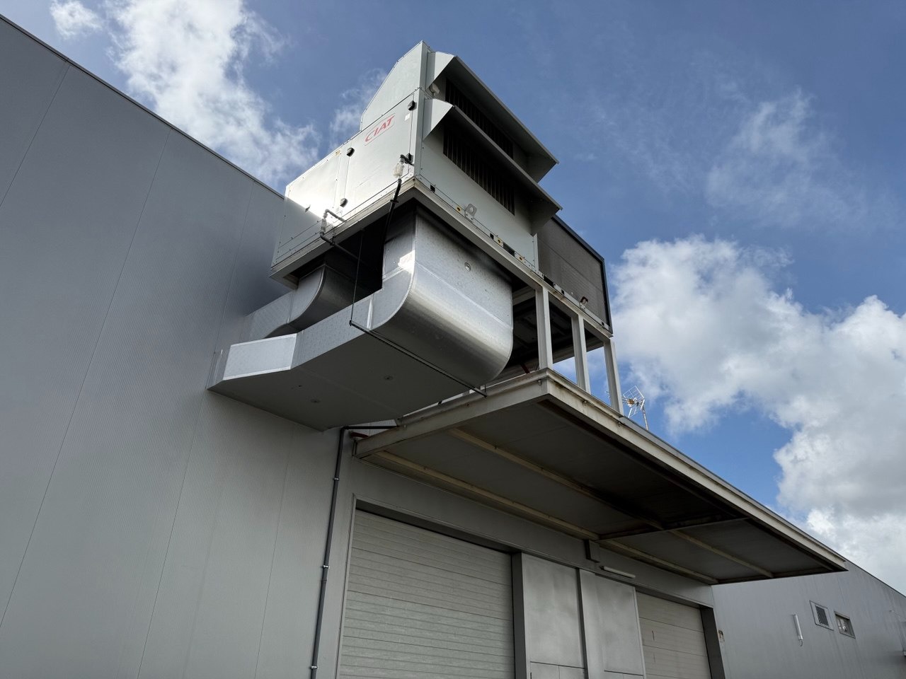 Zewnętrzna instalacja klimatyzacyjna CIAT na budynku przemysłowym, widok z dołu, niebieskie niebo z chmurami w tle. Metalowe kanały wentylacyjne.