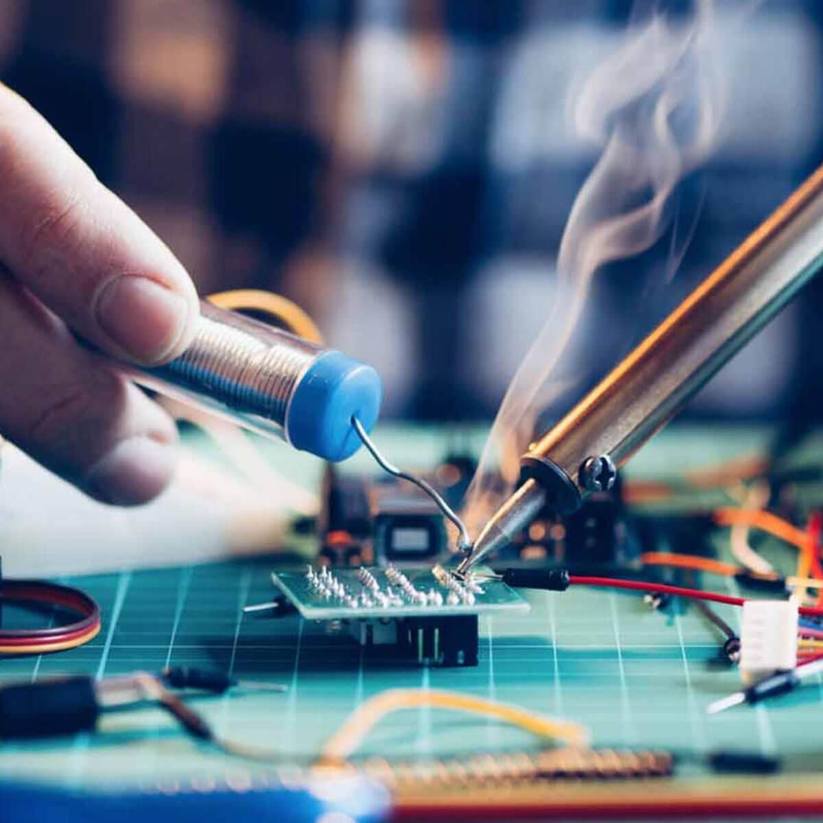 Precyzyjne lutowanie elementu elektronicznego na zielonej płytce drukowanej, z dymem unoszącym się znad grota lutownicy. Widoczne przewody i cyna.