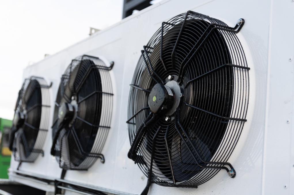 Biała obudowa klimatyzatora z trzema wentylatorami w czarnych osłonach, widoczne z bliska pod kątem, z kroplami wody na obudowie.