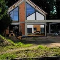 AS BUD DEVELOPMENT SPÓŁKA Z OGRANICZONĄ ODPOWIEDZIALNOŚCIĄ - Nowoczesny dom w trakcie budowy: ściany z cegły, duże okna, surowy beton, widoczne zbrojenia. Częściowo wykończona elewacja i otoczenie w stanie surowym.