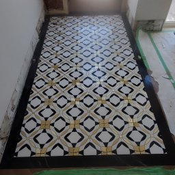 Soldatke Łazienki - Wzorzysta podłoga z płytek w trakcie układania, widoczne zabezpieczenia i narzędzia. Nietypowy wzór z motywem rombów i złotymi akcentami.