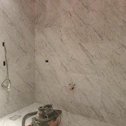 Soldatke Łazienki - Łazienka w trakcie prac: marmurowe płytki na ścianach i podłodze, widoczne kable, rury i odkurzacz przemysłowy. Etap prac wykończeniowych.