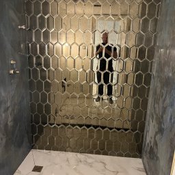 Soldatke Łazienki - Wykończona kabina prysznicowa z heksagonalnymi, lustrzanymi płytkami na ścianie i marmurową podłogą z odpływem liniowym. Widoczne elementy armatury.