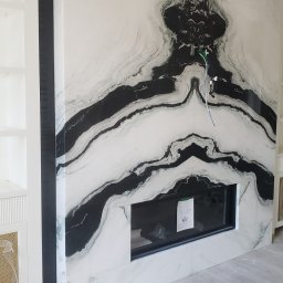 Soldatke Łazienki - Ściana wykończona białym marmurem z czarnymi żyłami, wbudowany czarny wkład kominkowy, widoczne przewody elektryczne. Nowoczesne wykończenie wnętrza.