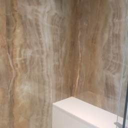 Soldatke Łazienki - Wykończona łazienka z beżowymi płytkami imitującymi marmur na ścianach, białą zabudową i podłogą z jasnych płytek. Widoczny fragment kabiny prysznicowej.